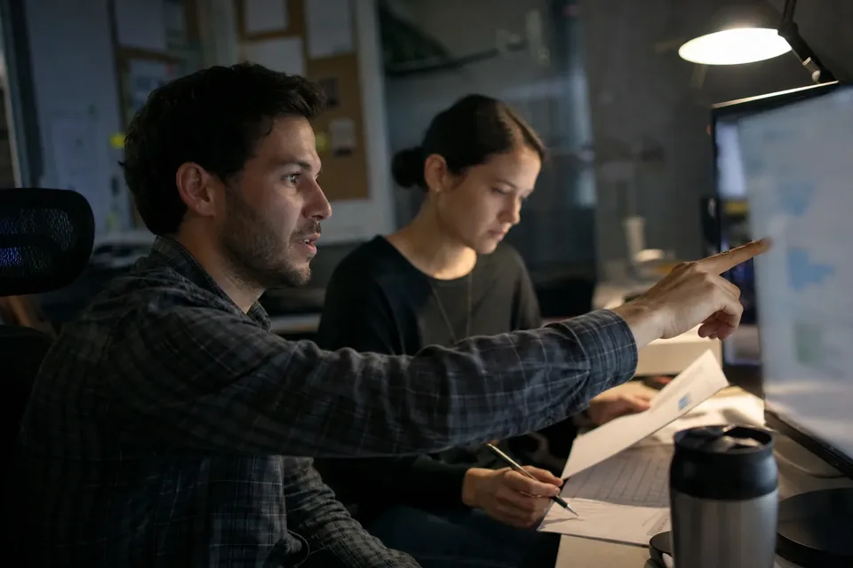 Trust and safety analyst flagging a suspicious account with a colleague taking notes