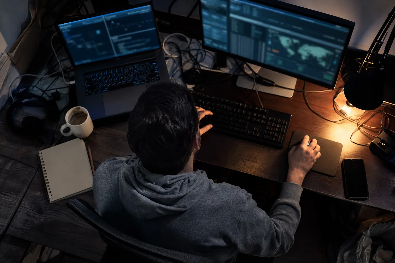 Overhead view of a security analyst's desk at night with a laptop, monitor and keyboard