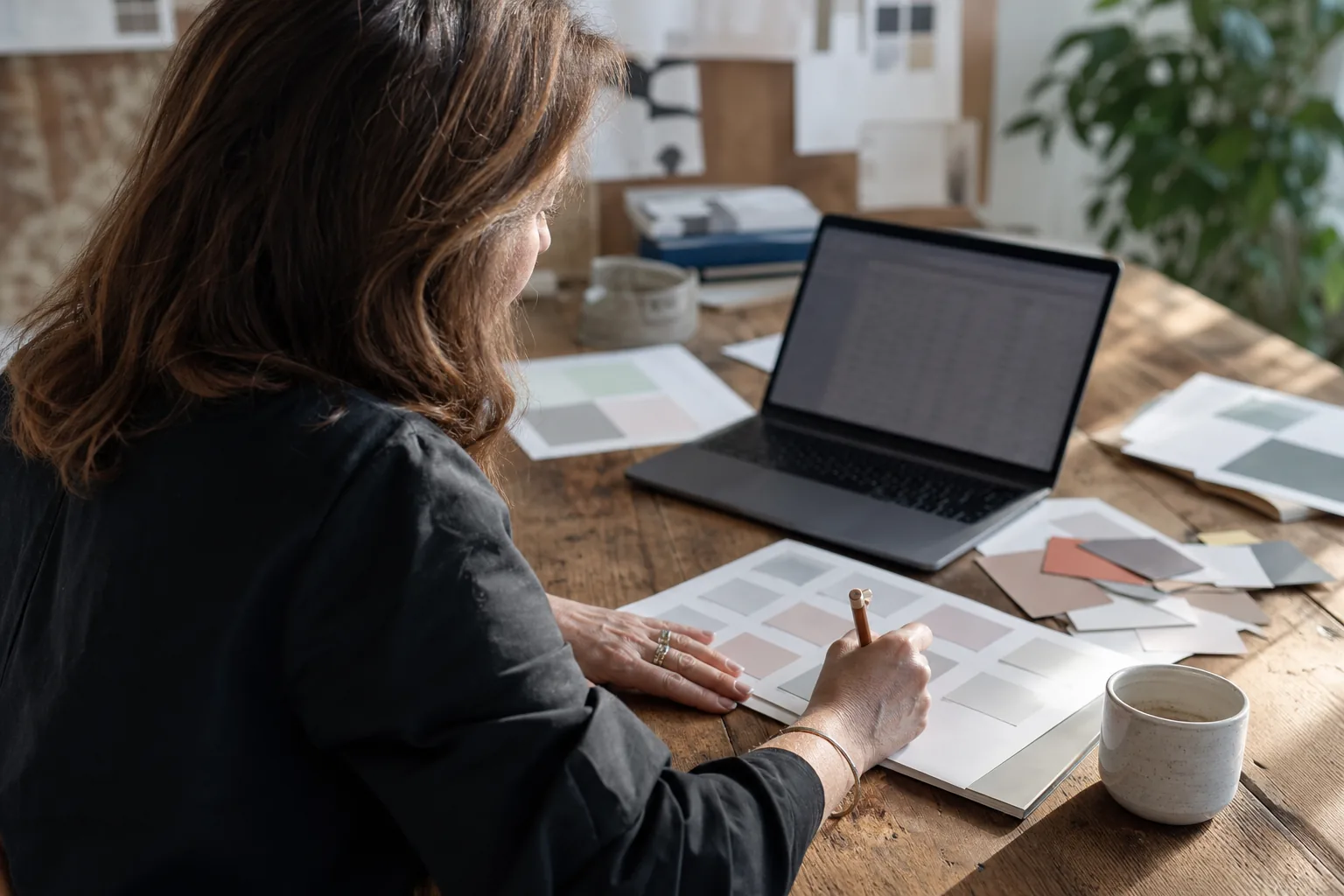 Naming consultant reviewing a printed grid of candidate brand names with a laptop of search results beside it