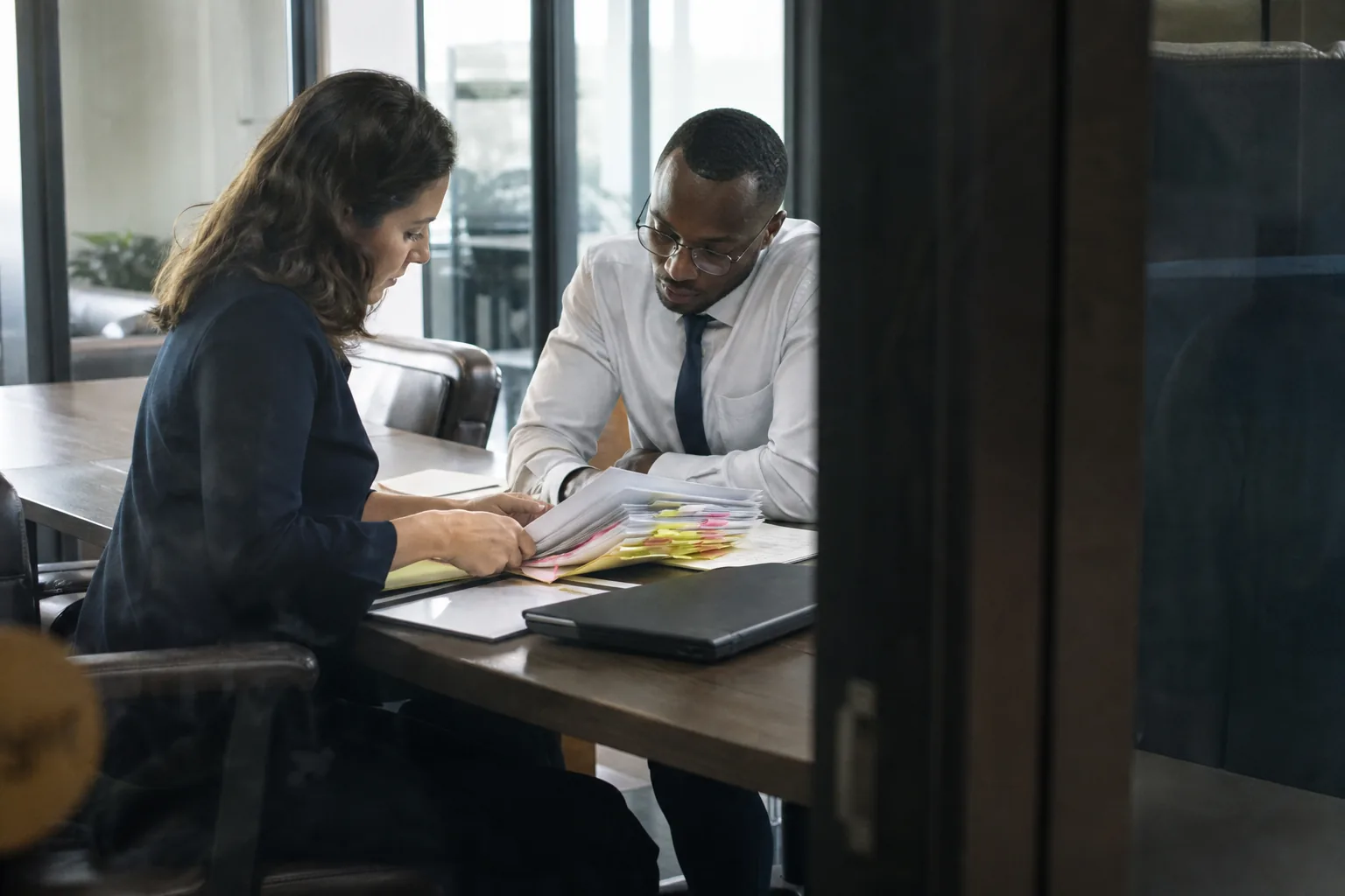 Two adult analysts reviewing printed case files together at a meeting table in a quiet office