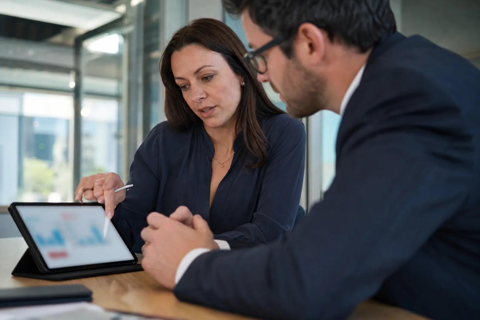 Head of brand protection discussing a chart on a tablet with a finance director in a meeting room